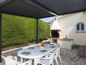 Une terrasse extérieure avec une table ronde pour quatre personnes, un barbecue et un mur blanc agrémenté d’une fenêtre.