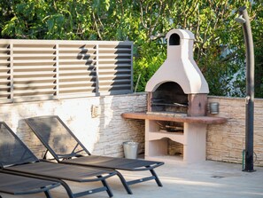 Un área de estar al aire libre con pared de piedra, una parrilla y una cerca de metal.