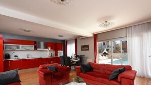 A modern living room with red sofas, a glass coffee table, and a view of a pool through large windows. - Vacation home Jure by Interhome (Zadar)