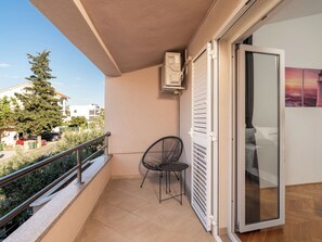 A balcony with a chair, a sliding glass door, and a view of the street and buildings.