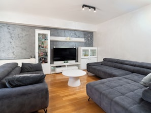 Una sala de estar moderna con sofás grises, un televisor de pantalla plana, una mesa de centro blanca y un mueble bar.