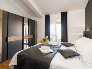 Habitación de hotel moderna con una cama grande, una mesita de noche con una bandeja de desayuno y vistas al exterior.