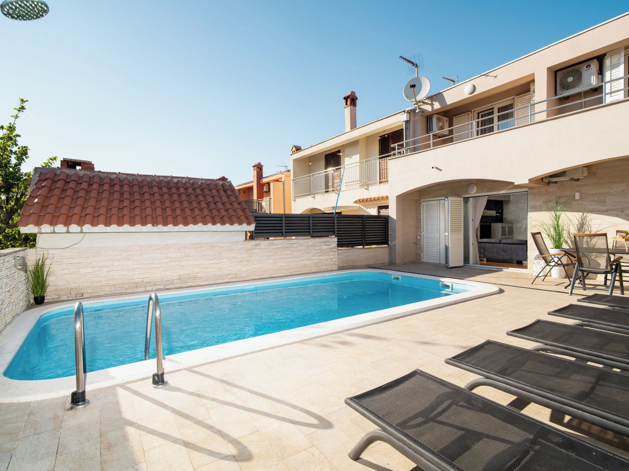 A swimming pool with a tiled deck, lounge chairs, and a building with balconies and satellite dishes.