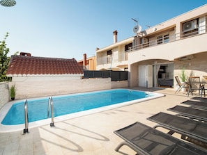 A swimming pool with a tiled deck, lounge chairs, and a building with balconies and satellite dishes.