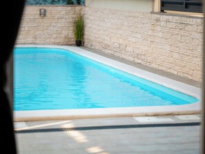 Una piscina rectangular con una pared de piedra en un lado y una zona de sol con baldosas.