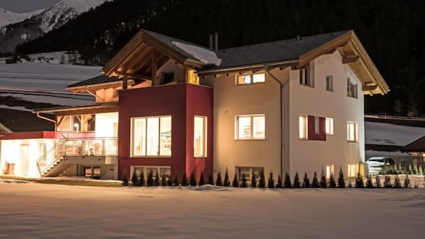 A two-story chalet with a snow-covered roof and a ski slope in the background. - Bella Monte by Interhome (Pettneu am Arlberg)