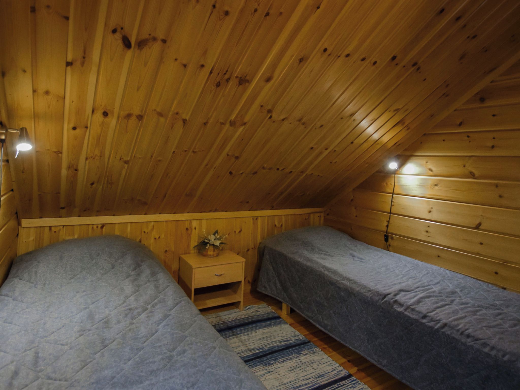 A small, wooden room with two single beds, a nightstand, and a lamp.