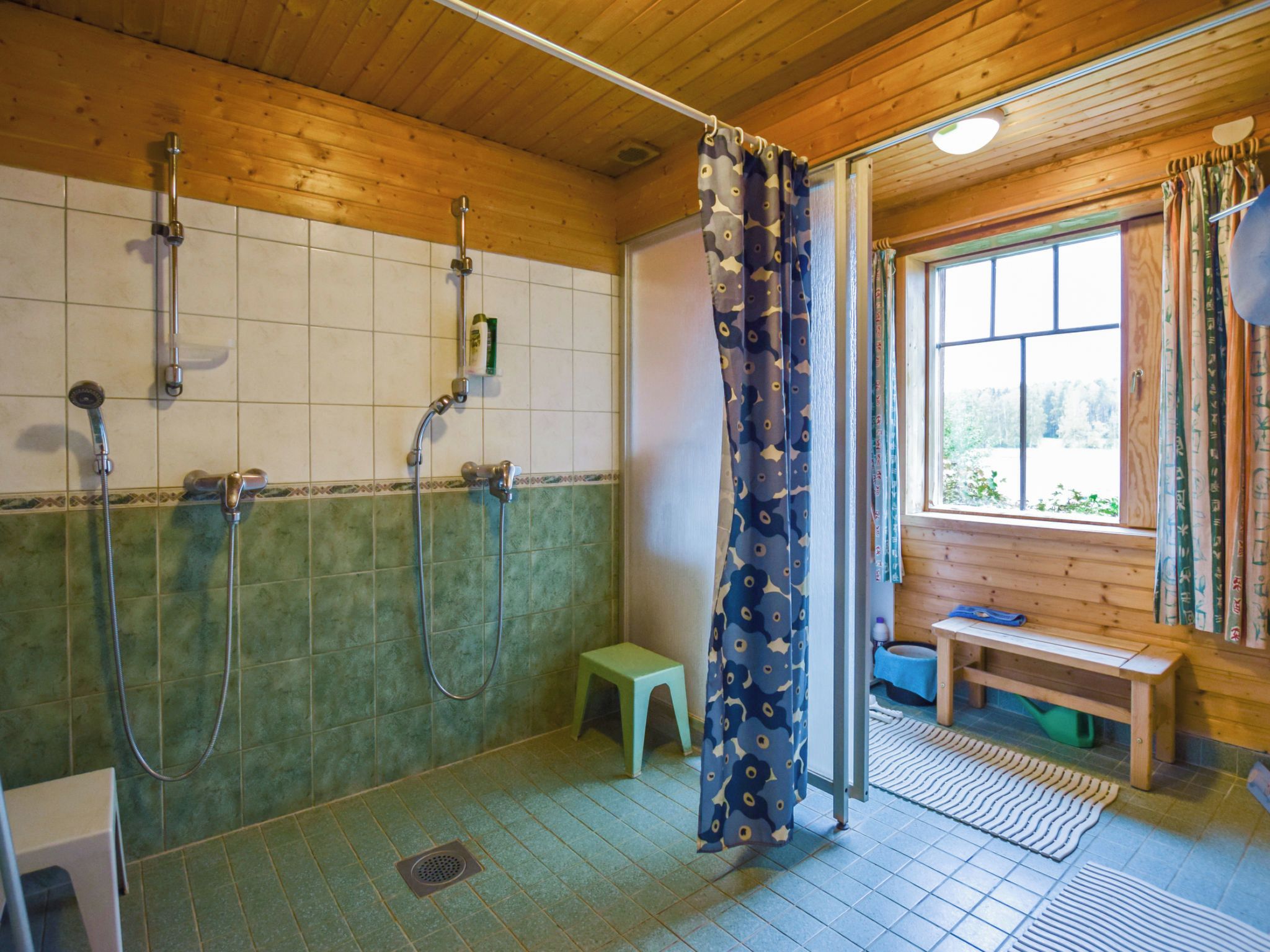 A shower area with multiple showerheads, a small stool, and a bench near a window.