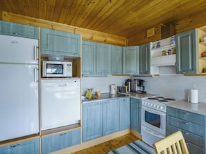 A compact kitchen with a refrigerator, microwave, stove, and sink. - Vuorimaja by Interhome (Ristiina)