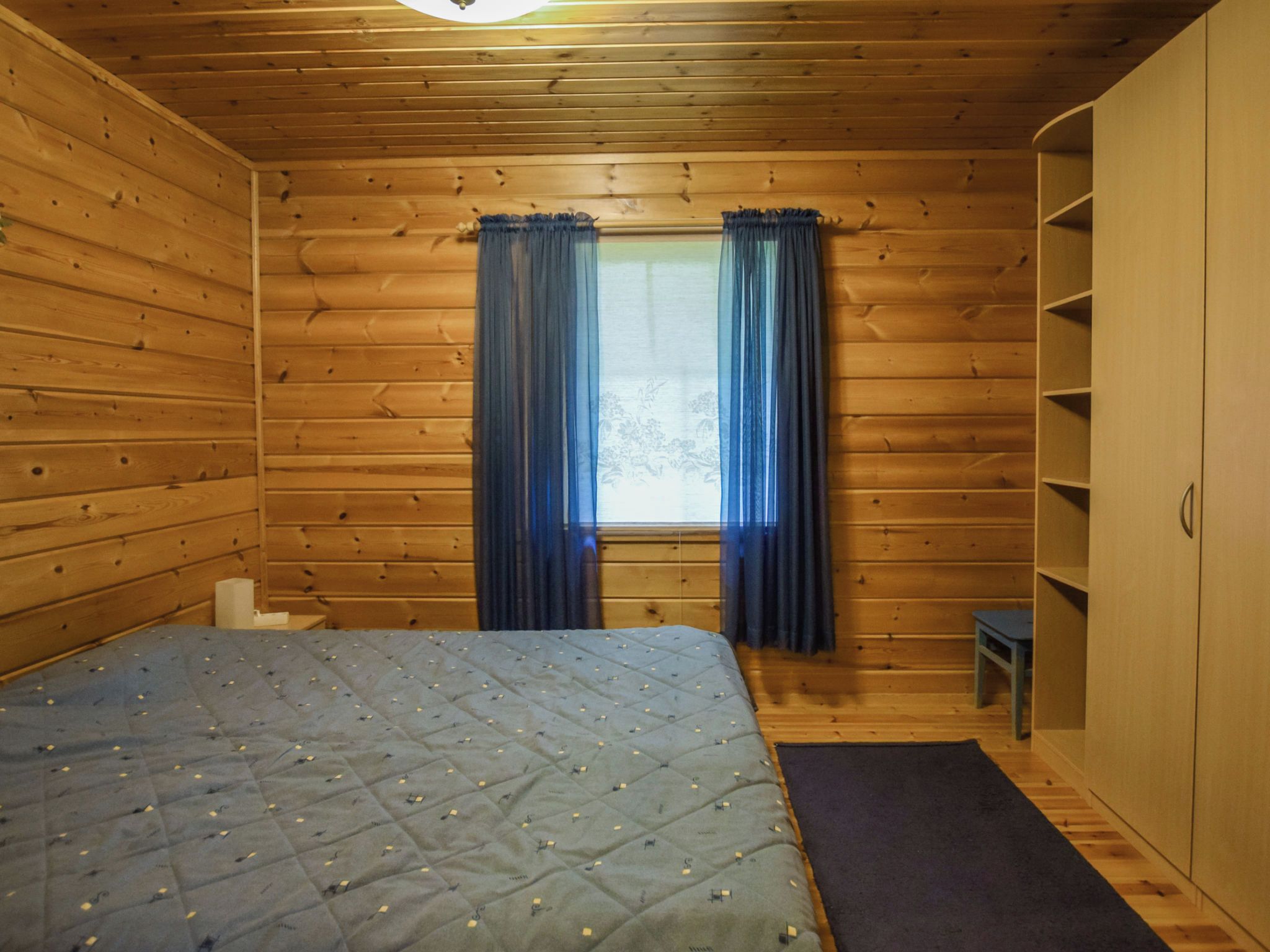 A wooden room with a bed, a window with curtains, and a wardrobe.