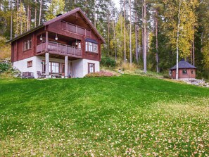 A two-story wooden cabin with a balcony, surrounded by a grassy yard and a forest. - Vuorimaja by Interhome (Ristiina)