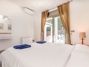 A bedroom with a large bed, a radiator, an air conditioning unit, a window with curtains, and a lamp. - Palmbeach by Interhome (Lloret de Mar)