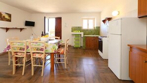 Ein Essbereich mit einem Tisch für vier Personen, Holzsesseln, einem an der Wand befestigten Fernseher und einer Küche mit Kühlschrank und Spüle.