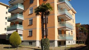 Ein mehrstöckiges Wohnhaus mit Balkonen, einer Palme und einem ordentlich geschnittenen Busch.