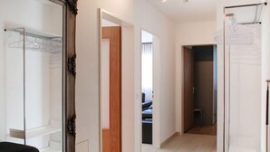 Ein modernes Hotelzimmer mit einem großen Spiegel, einem schwarzen Sofa, einer Holztür und Blick in ein weiteres Zimmer.