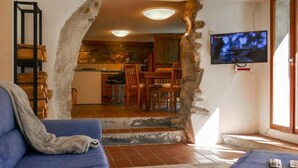 Una sala de estar con un sofá azul, un televisor montado en la pared y una cocina visible a través de un arco de piedra.