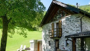 Una casa de piedra con balcón, un porche pequeño y un jardín con sillas.