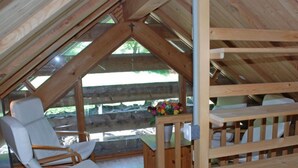 Un interior de madera con techo inclinado, una silla blanca acolchada, un banco de madera y una pequeña mesa con un jarrón de flores.