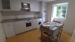 Una cocina compacta con armarios blancos, horno empotrado, lavadora y comedor con mesa dispuesta para cuatro.