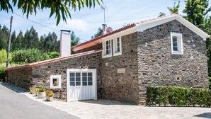 Una casa de piedra con techo rojo, puerta blanca y un pequeño jardín con plantas en macetas.