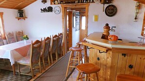 Et rustikt interiør med et område med træbar, et spisebord med stole og et ur på væggen.