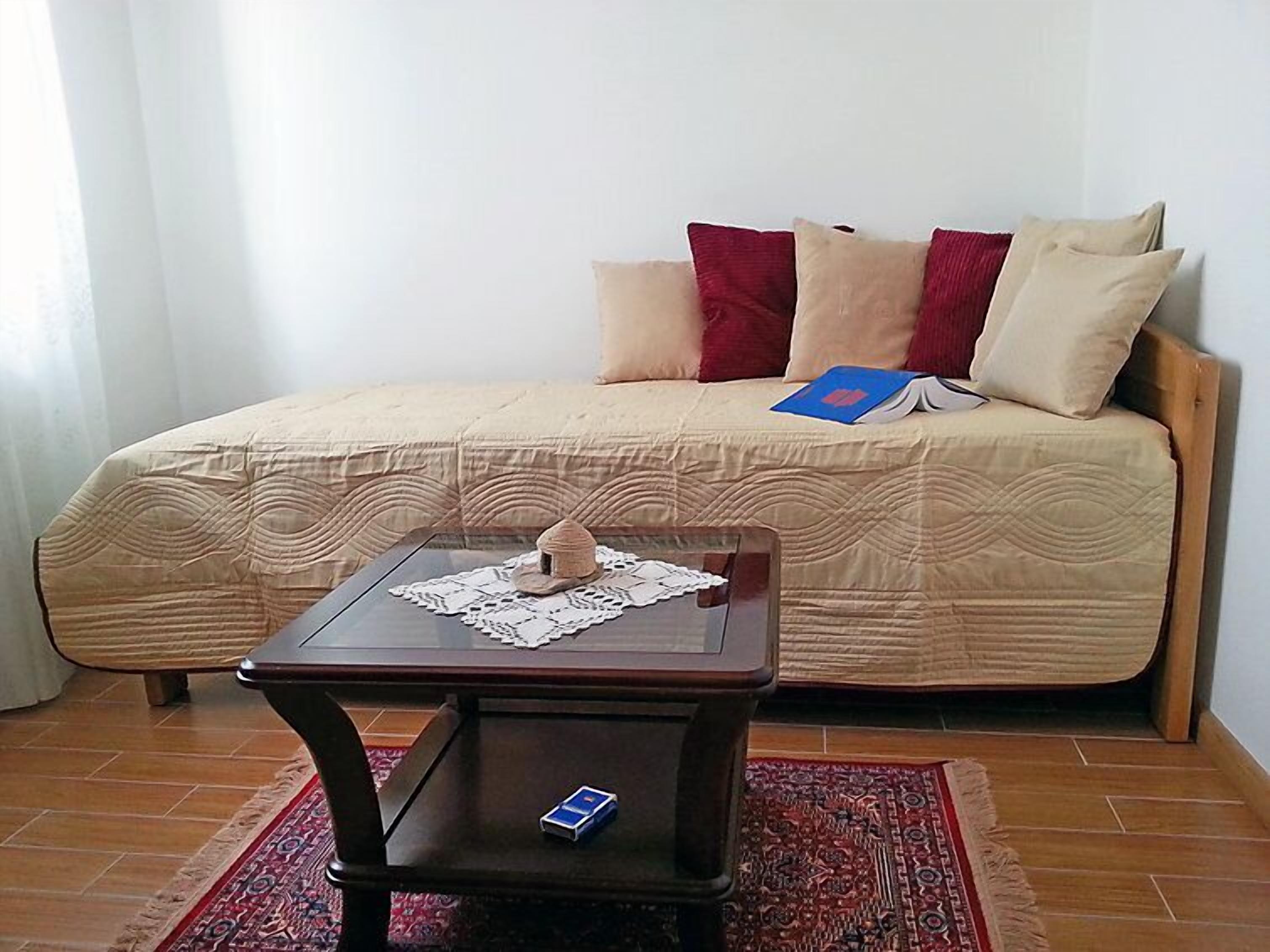 Une pièce avec un lit, une petite table sur laquelle se trouvent un chapeau et un livre, et un tapis à motifs.