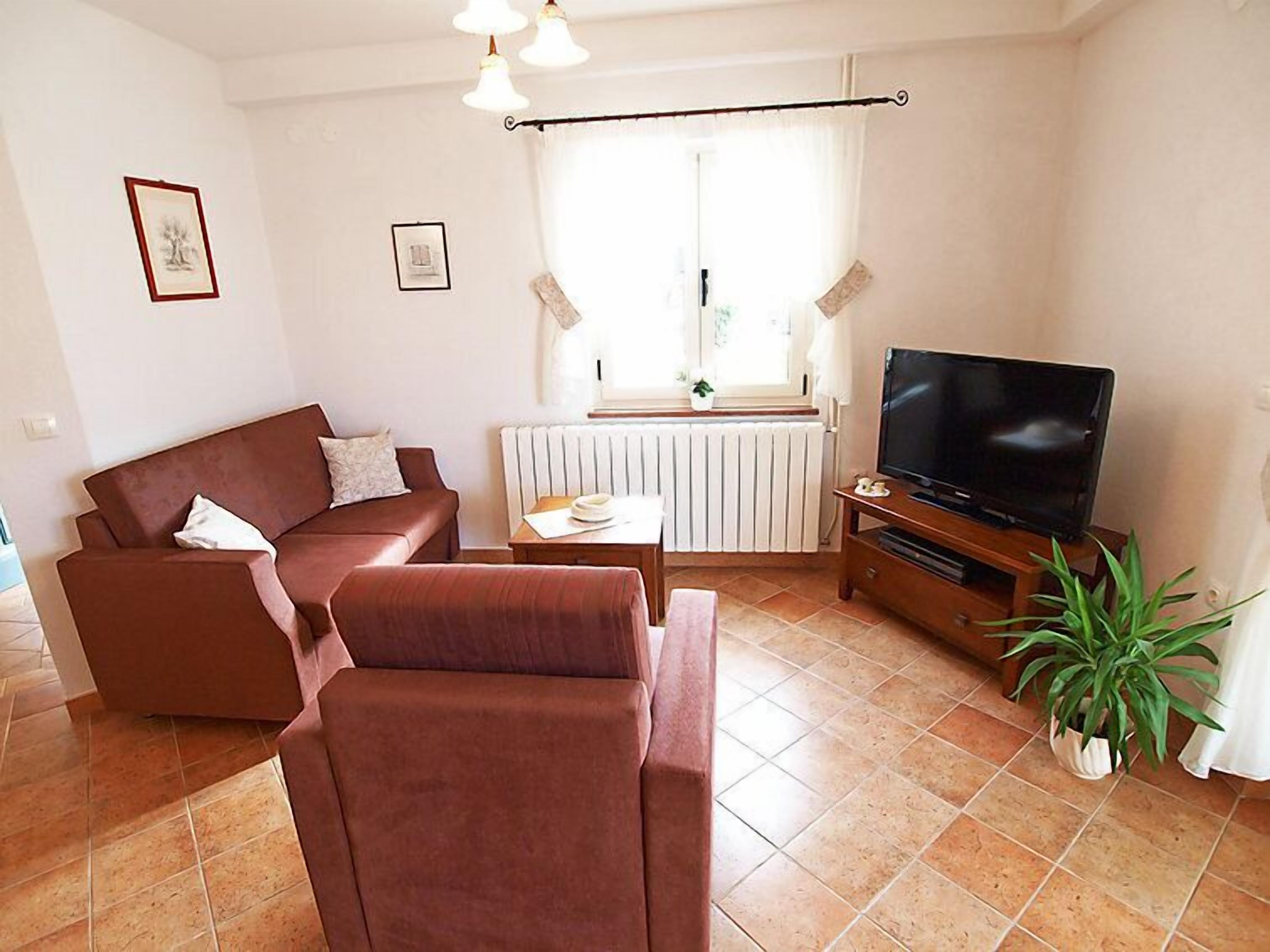 A living room with a brown sofa, a coffee table, a TV on a wooden stand, and a potted plant.