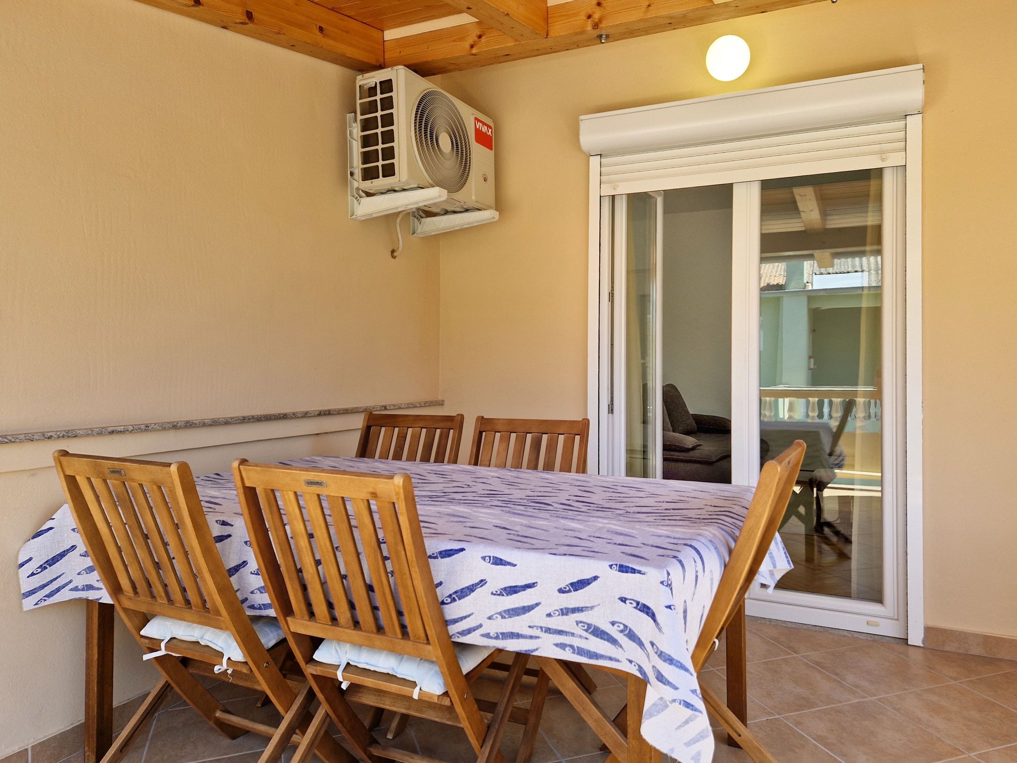 Un coin repas avec une table et des chaises, un appareil de climatisation et une porte-fenêtre coulissante donnant sur un balcon.