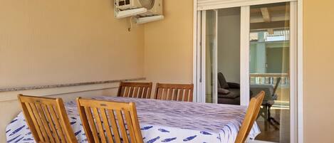 Un coin repas avec une table et des chaises, un appareil de climatisation et une porte-fenêtre coulissante donnant sur un balcon.