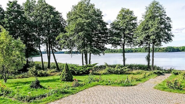 A paved pathway leading to a lake with trees and greenery on either side. - Głęboczek 21 by Interhome (Gleboczek)