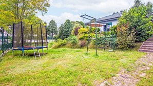 A grassy backyard with a trampoline, a swing set, and a house in the background. - Głęboczek 21 by Interhome (Gleboczek)