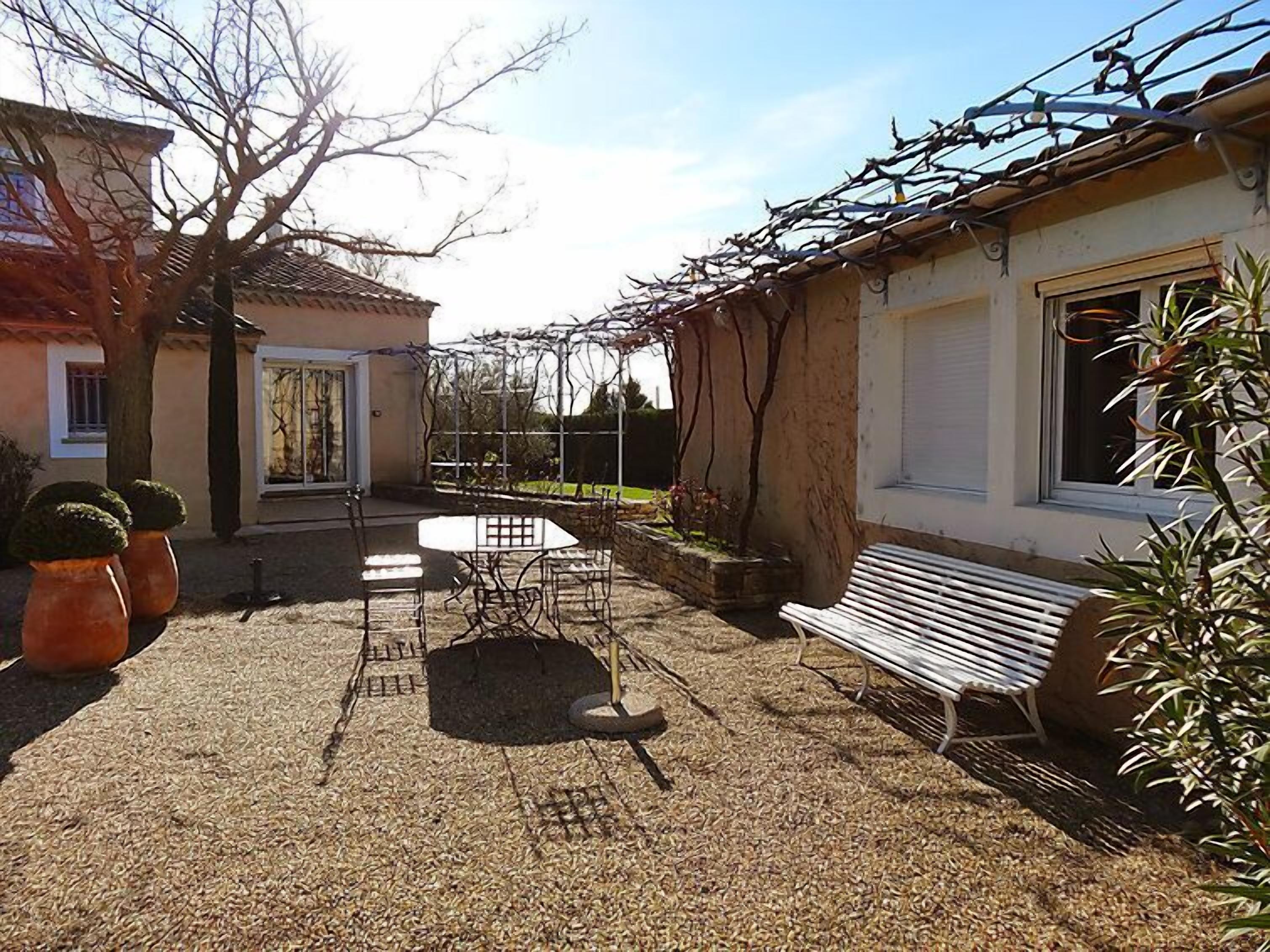 Un patio con mesa y sillas, un banco y plantas en macetas.