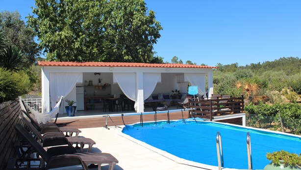 A pool area with lounge chairs, a covered seating area, and a view of the surrounding landscape.