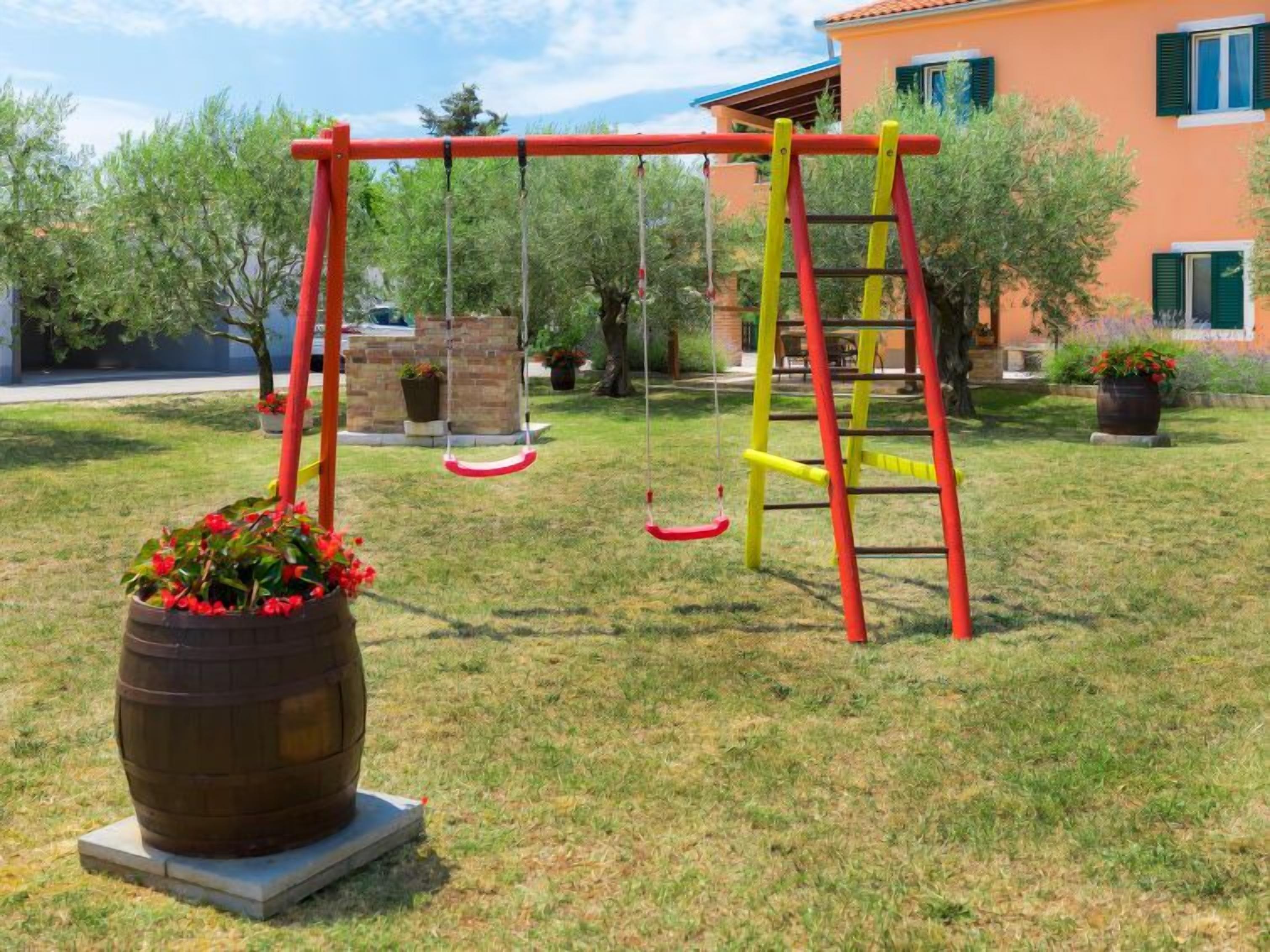A playground with swings and a ladder, surrounded by grass and potted plants.