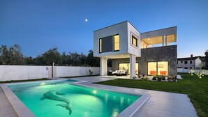 Een modern huis met twee verdiepingen, een zwembad, een terras en een verzorgd gazon.