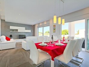 A modern dining area with a red tablecloth, white chairs, and a TV in the background.
