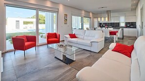 Een moderne woonkamer met een witte bank en rode stoelen, een glazen salontafel, en grote schuifpuien die leiden naar een balkon.