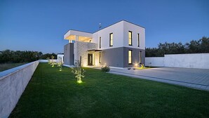 Een modern huis met twee verdiepingen, een plat dak, grote ramen en een verzorgd gazon.