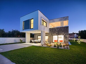 A modern two-story house with a flat roof, large windows, and a well-maintained lawn.