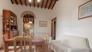 A dining area with a wooden table and chairs, a white sofa, and a kitchen in the background. - Ca' di Bacco by Interhome (Cortona)