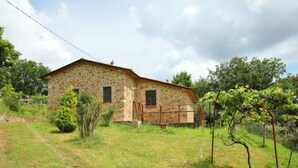 A stone house with a sloped roof, a small porch, and a garden with grass and a few trees. - Ca' di Bacco by Interhome (Cortona)