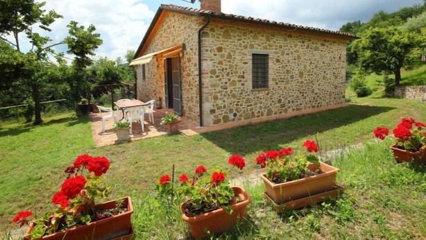 A stone house with a chimney, a small patio with a table and chairs, and potted geraniums in the foreground. - Ca' di Bacco by Interhome (Cortona)