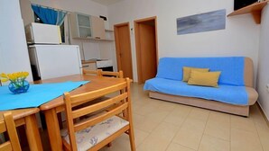 Un ambiente compatto con angolo ristoro, angolo cottura e divano.