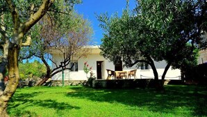 Un edificio bianco con un muro in pietra, un prato verde e un tavolo con sedie di fronte.