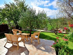 An outdoor patio area with wicker furniture and a stone-tiled floor, surrounded by lush greenery and flowering plants. - Vacation home Keti by Interhome (Brač/Sumartin)