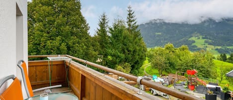 A balcony with a wooden railing, a glass table, and orange chairs.