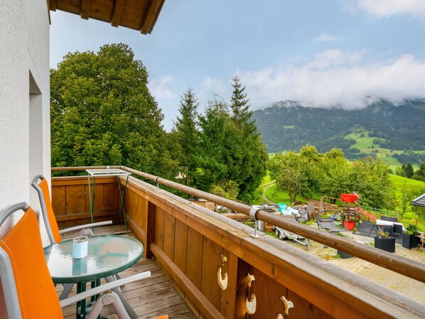 A balcony with a wooden railing, a glass table, and orange chairs.