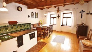 A rustic kitchen with wooden beams, a dining area with a table and chairs, and a small altar with religious icons.