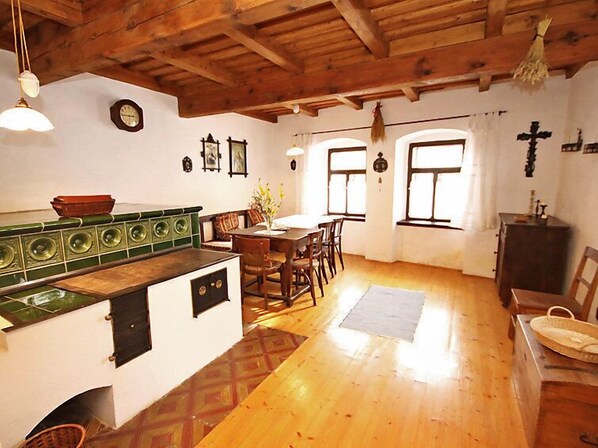 A rustic kitchen with wooden beams, a dining area with a table and chairs, and a small altar with religious icons.