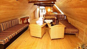 A cozy attic room with wooden walls and a sloped ceiling. It features a long sofa, two armchairs, and a small table.